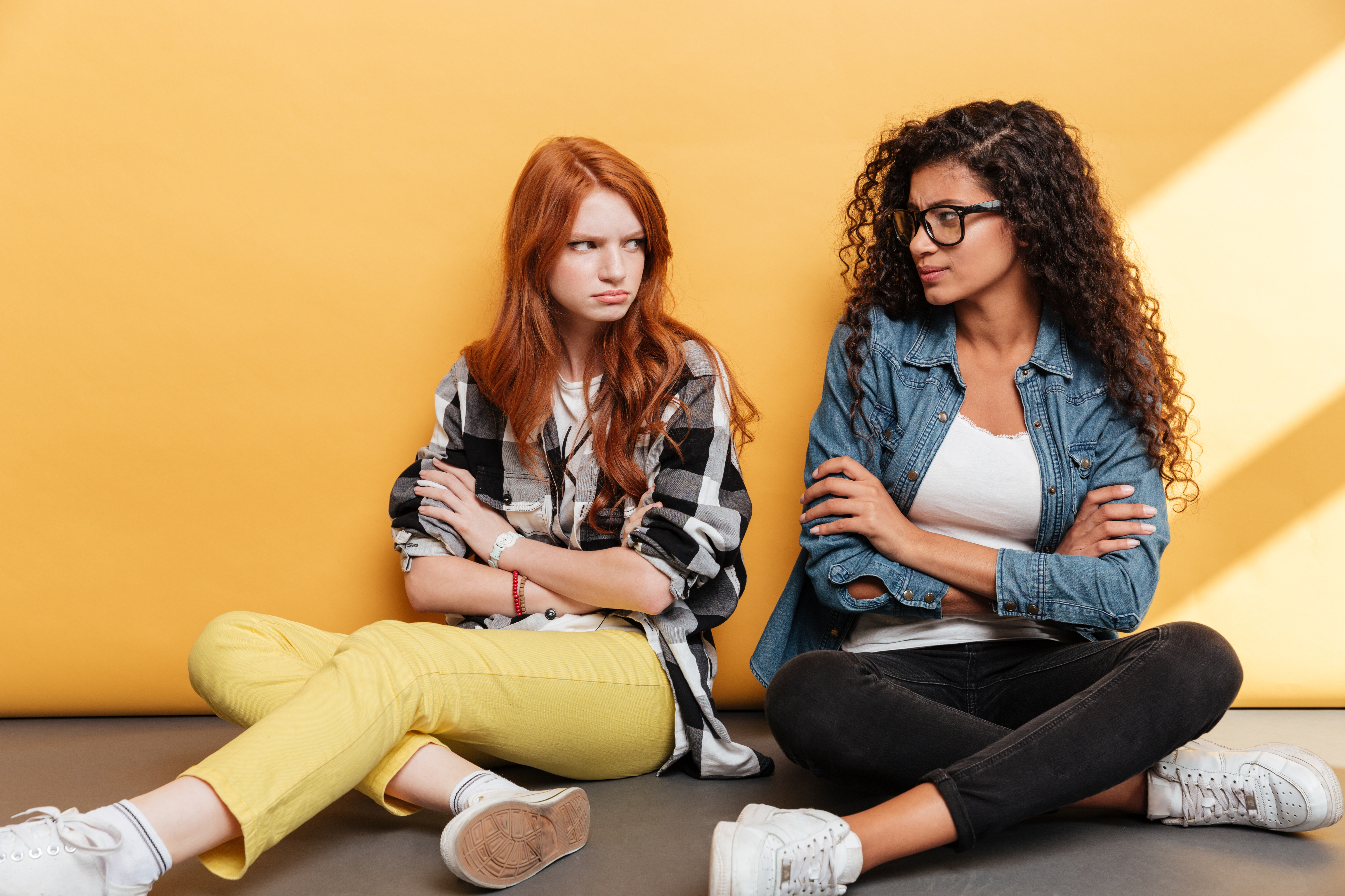 Two sad offended young women sitting with arms crossed