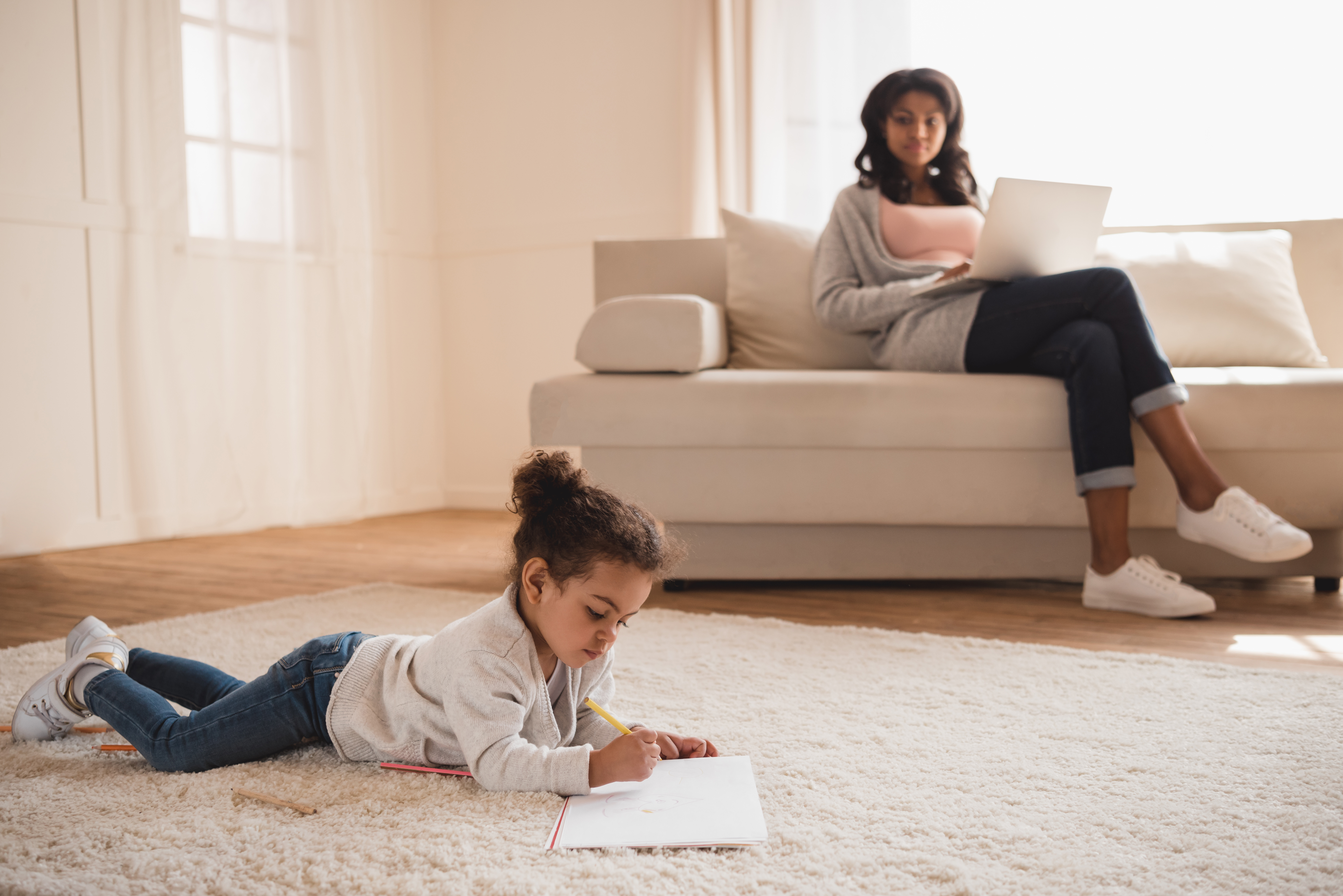 Mother using laptop while cute little daughter drawing