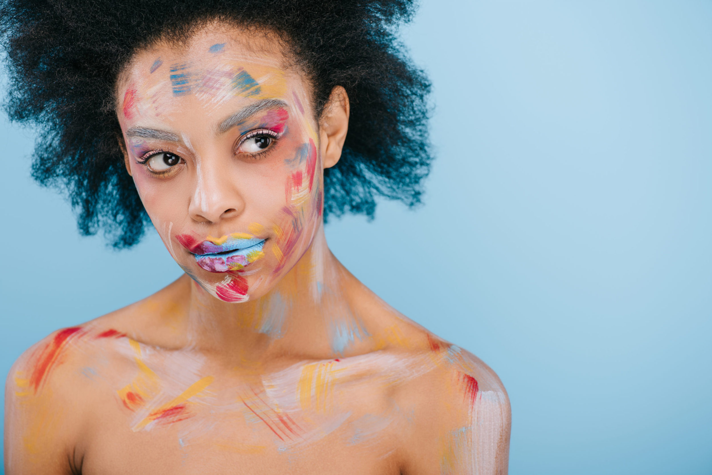 attractive young woman with paint strokes on face looking away isolated on blue